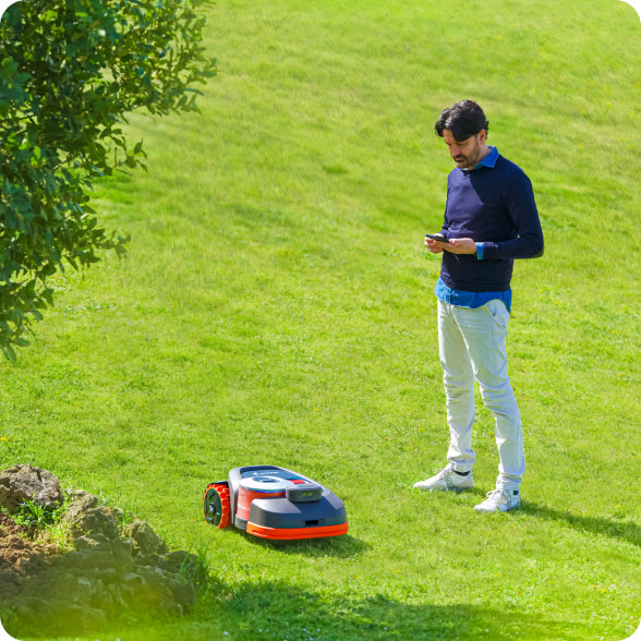 Man uses phone with Navimow i105E robot lawn mower outside.