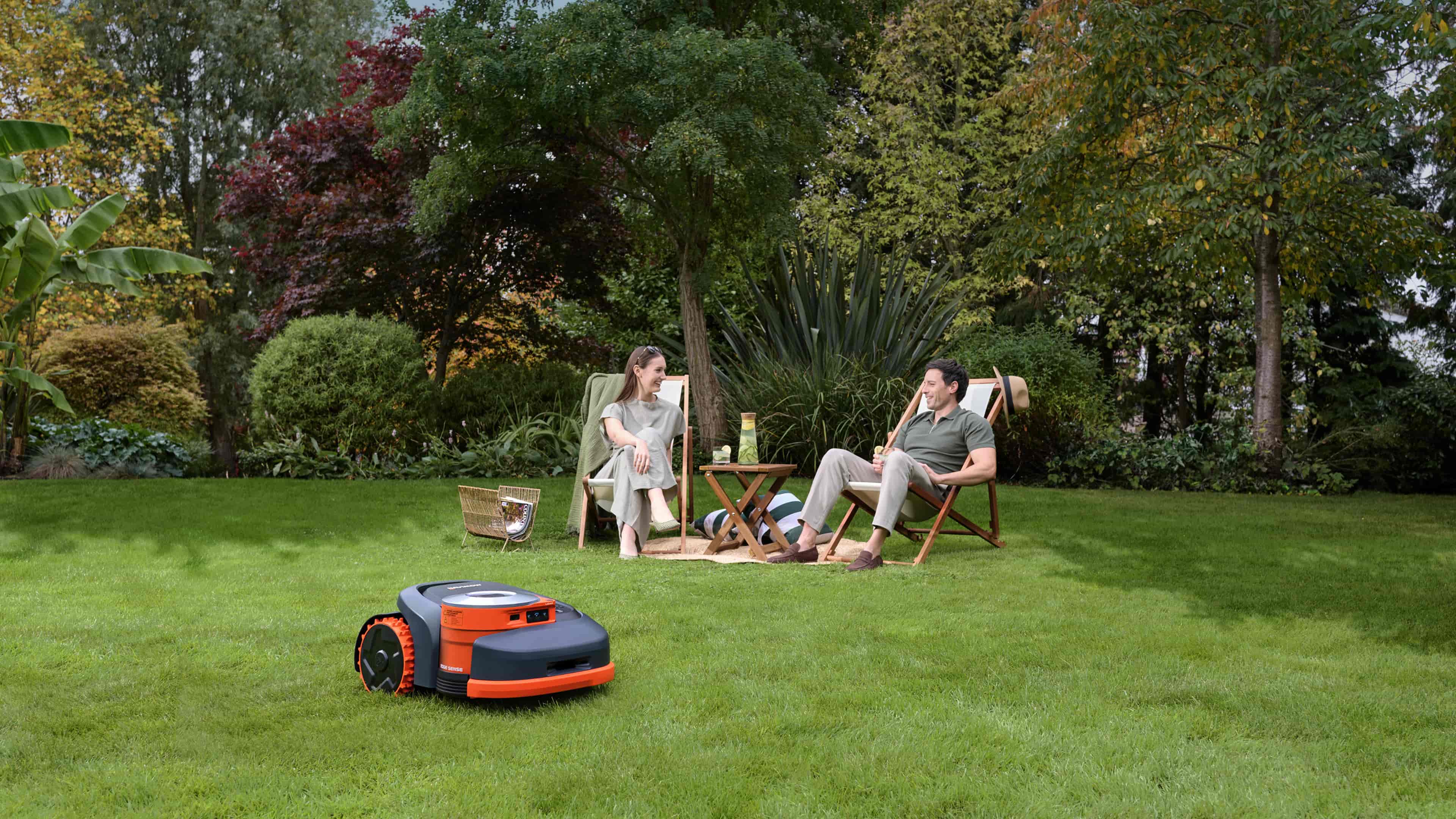 Navimow i110E robot lawn mower mows grass while two people sit.