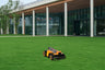 Navimow i110E robot lawn mower on grass near glass building.