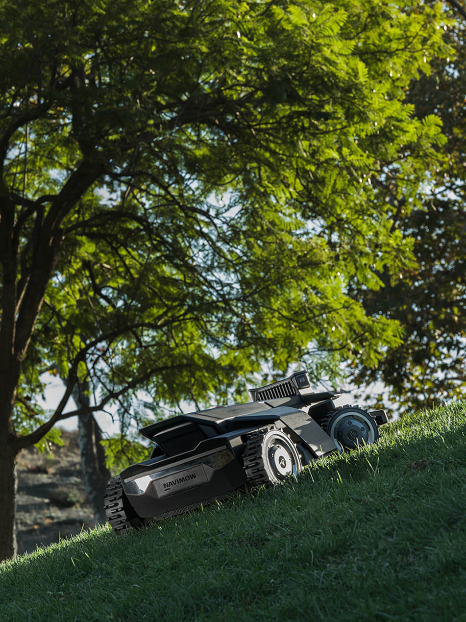 Navimow i110 robot lawn mower climbs up a grassy hill.