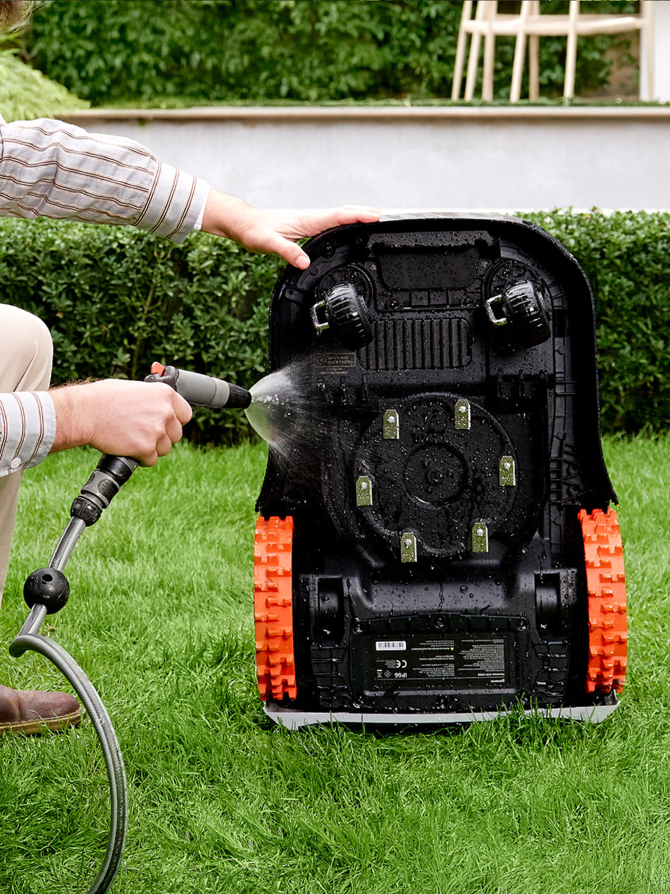 Navimow i110N robot lawn mower being cleaned with a hose.