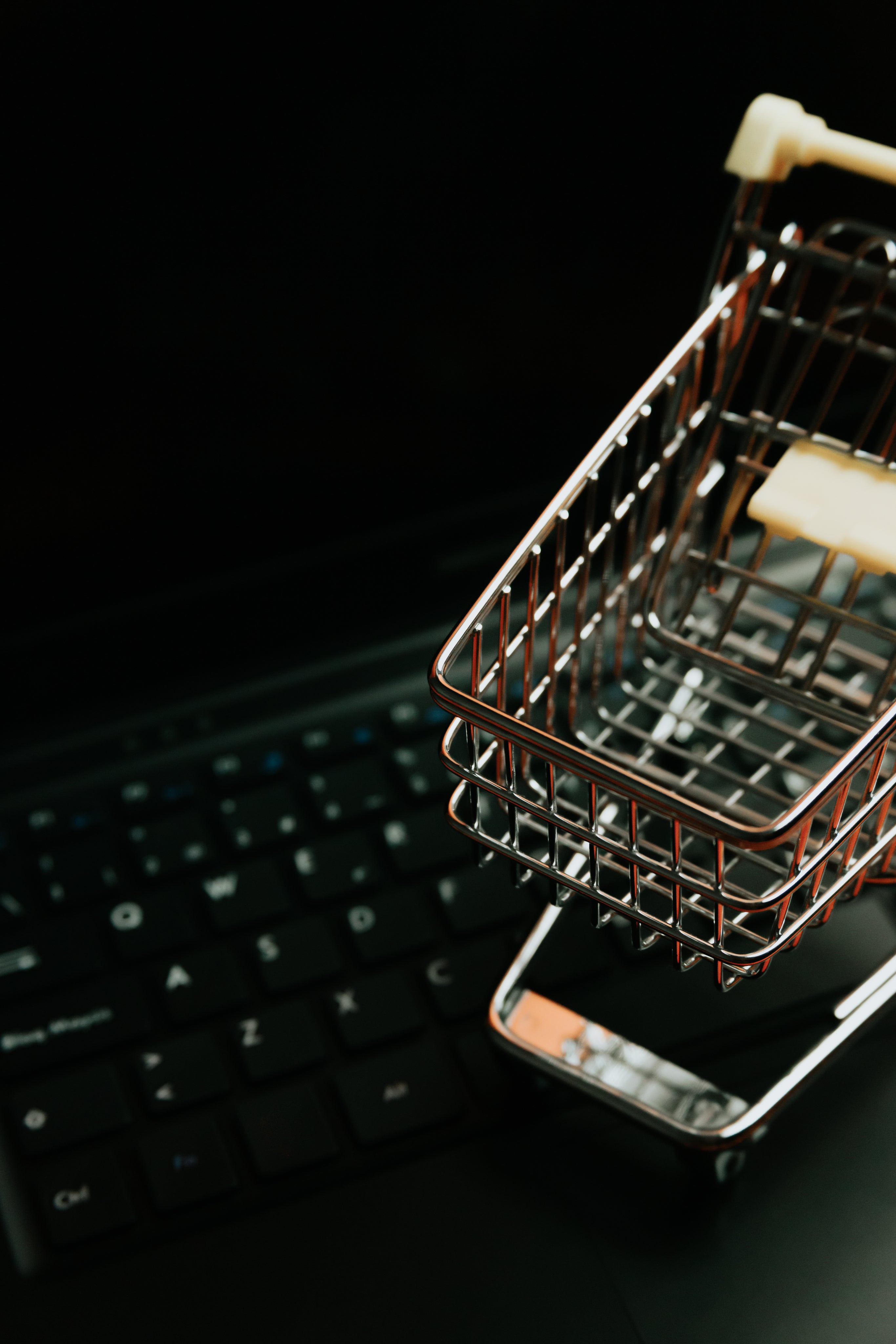 Small metal shopping cart on a black laptop computer keyboard.