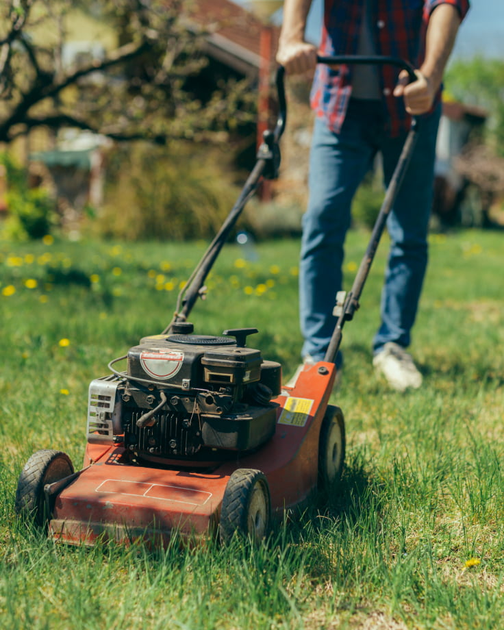 Man pushes a red gas powered mower through the grass.