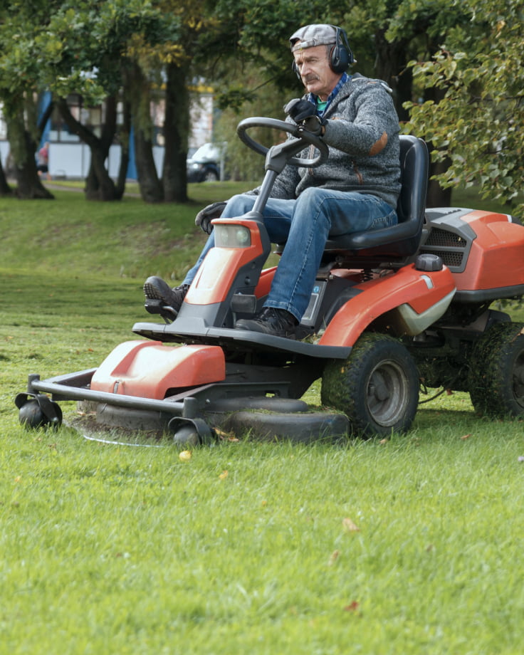 A man is riding a red lawn mower on grass.