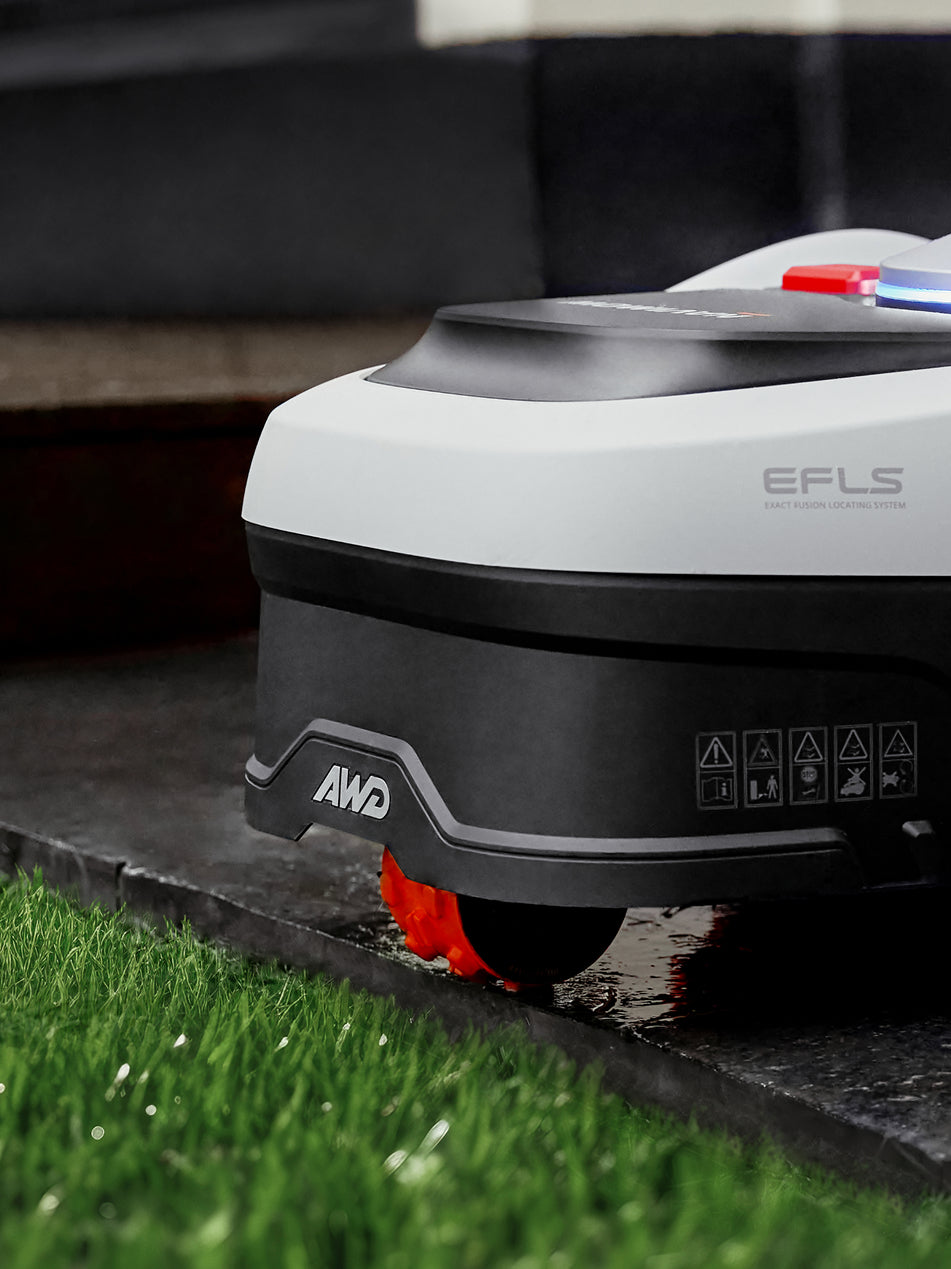 Navimow H1500E robot lawn mower on wet pavement by grass.