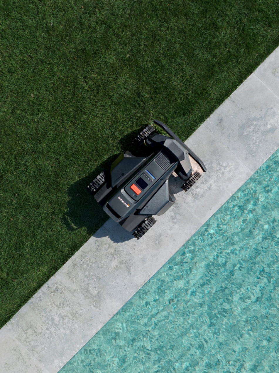 Navimow i105E robot lawn mower on grass near a pool.
